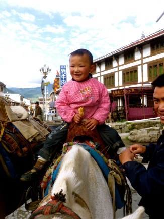 A man puts his baby on my horse as we're waiting to start a horse trek in Songpan, Sichuan